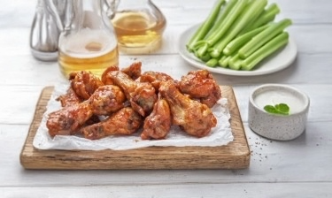 Tray of buffalo chicken wings with a mug of beer and plate of celery in the background.